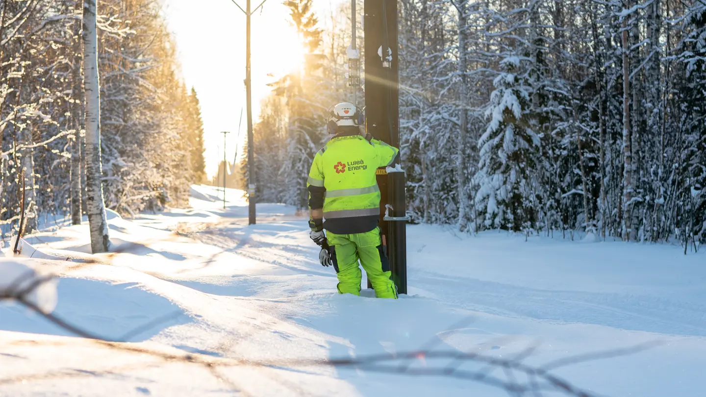 Person i varselkläder bredvid en elkraftstolpe. Vinter